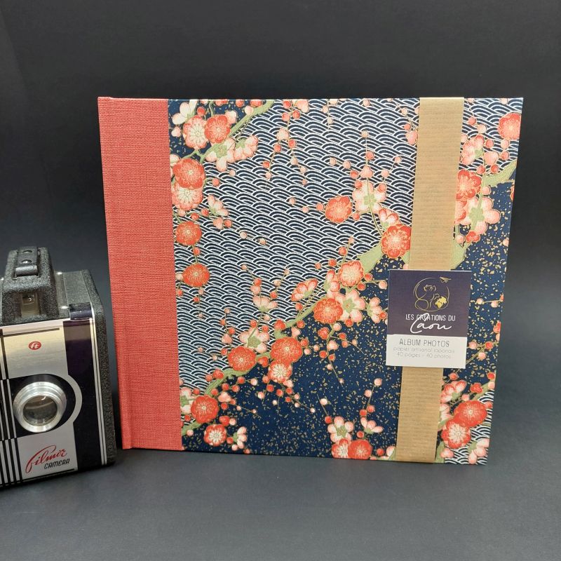 Album photos pouvant accueillir jusqu'à 40 photos recouvert d'un papier japonais bleu aux motifs de vagues blanches et de fleurs de prunier roses et rouges.